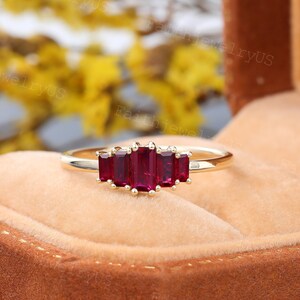 May include: A gold band ring with five emerald-cut ruby gemstones. The ring is set in a classic style and features a delicate band.