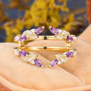 May include: A gold ring guard featuring two open bands connected by leaf-shaped metalwork. The design is accented with marquise-cut purple amethyst stones, small round white accent stones, and small round opals at the outer ends of the leaves.