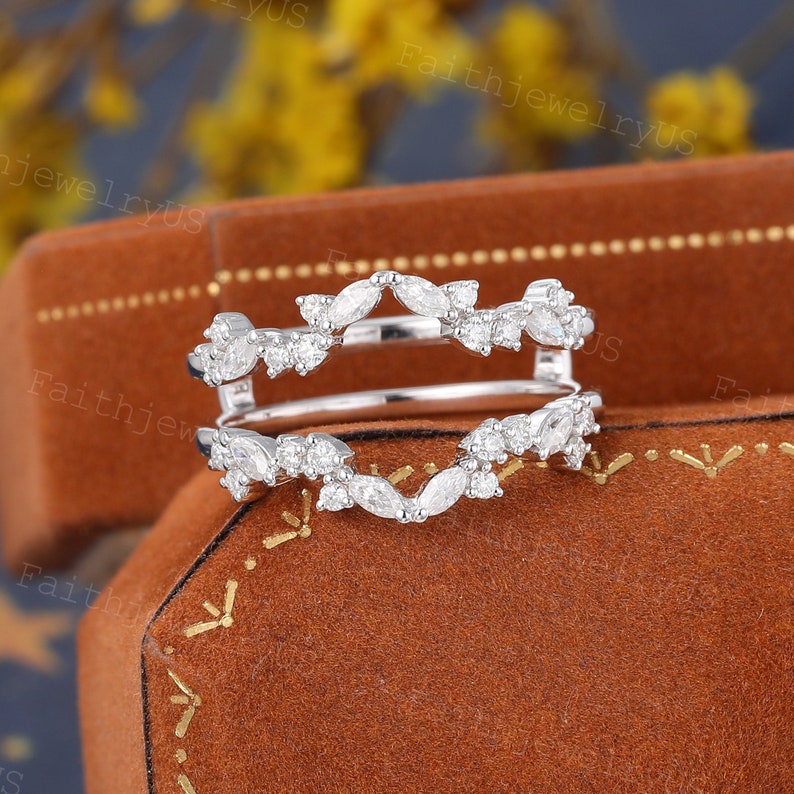 May include: A delicate silver ring enhancer with a marquise and round diamond design. The enhancer is set on a brown velvet background.