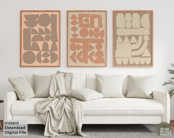 May include: Three abstract art prints with geometric shapes in shades of beige and peach. The prints are framed in natural wood and hung on a white wall above a white couch.
