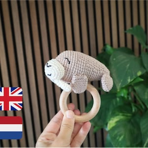 May include: A handmade crochet baby rattle in the shape of a seal. The seal is light brown with a white face and attached to a natural wooden ring. The rattle is designed for infants and toddlers.