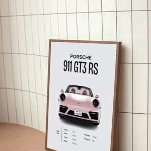 May include: A framed poster with a white background featuring a pink Porsche 911 GT3 RS. The poster includes the car's specifications, including the year, engine size, power, torque, 0-100 mph time, and top speed.