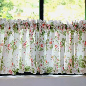 Puede incluir: Cortina floral blanca con un estampado de rosas rojas y hojas verdes. La cortina está hecha de una tela ligera y cuelga frente a una ventana. La cortina está fruncida en la parte superior, creando un efecto de volantes.