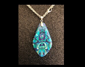 Puede incluir: Un collar con un colgante en forma de lágrima con una cadena de plata. El colgante está hecho de resina marmoleada azul, verde y morada.