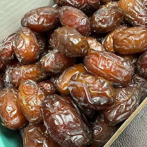 May include: A close-up of a box filled with dates. The dates are a deep brown color and have a shiny, glossy finish.