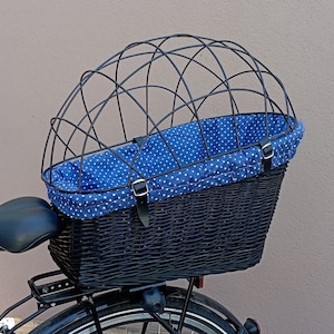 以下が含まれることがあります： 黒の籐製の自転車用バスケット。青と白のドット柄のライナーと、黒い金属製のケージトップが付いています。
