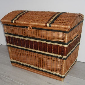 Puede incluir: Una cesta de almacenamiento de mimbre tejida grande con una tapa con bisagras. La cesta tiene un patrón de rayas marrones, negras y blancas.