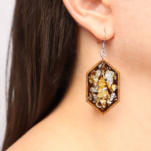 May include: Hexagon-shaped earrings with a wood frame and gold and silver leaf accents.