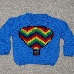 May include: A blue knitted sweater with a colorful hot air balloon design. The balloon is made of red, yellow, green, and blue yarn.