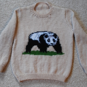 May include: A cream-colored knitted sweater with a black and white panda bear design on the front.