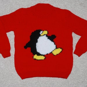 Può includere: Un maglione rosso lavorato a maglia con un motivo a pinguino. Il pinguino è nero, bianco e giallo. Il maglione ha maniche lunghe e scollo tondo. L'indumento è in tessuto a maglia.