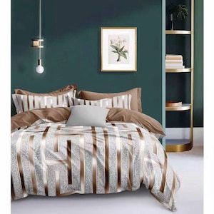 May include: A brown and silver geometric patterned duvet cover with two brown pillowcases and a white pillow. The bedding is on a bed with a teal green headboard and a gold bedside table.