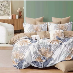 May include: White bedding with a tropical leaf pattern in shades of brown and grey. The bedding is arranged on a bed with a tan headboard and a white armchair in the background.