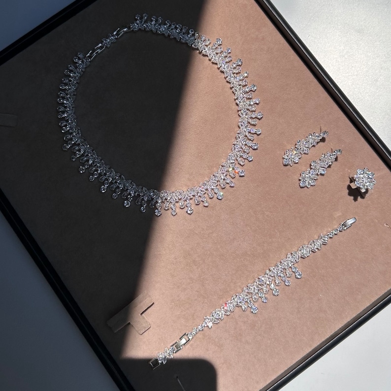 May include: A silver necklace, bracelet, and earrings set with clear crystal stones. The jewelry is displayed on a brown velvet background.