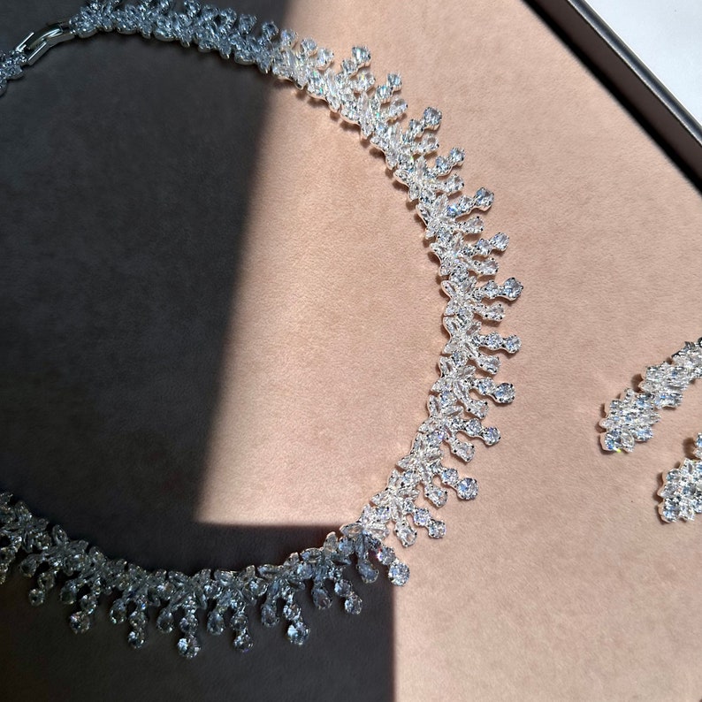 May include: A silver necklace and earrings set with a teardrop design, featuring clear sparkling stones.