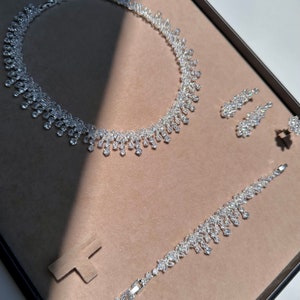 May include: A silver necklace, bracelet, and earrings set with clear crystal stones. The jewelry is displayed on a brown velvet background.