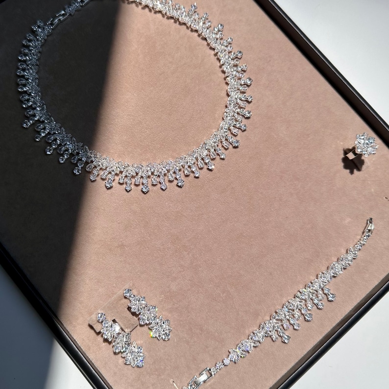 May include: A silver necklace and bracelet set with sparkling clear stones. The necklace is a delicate chain with a pendant that features a cluster of stones. The bracelet is a simple chain with a matching pendant.