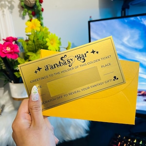 Puede incluir: Un boleto dorado de Fantasy Bar, con el texto "GREETINGS TO THE HOLDER OF THIS GOLDEN TICKET" y "SCRATCH OFF TO REVEAL YOUR FANTASY GIFT!". El boleto se sostiene sobre un sobre amarillo.