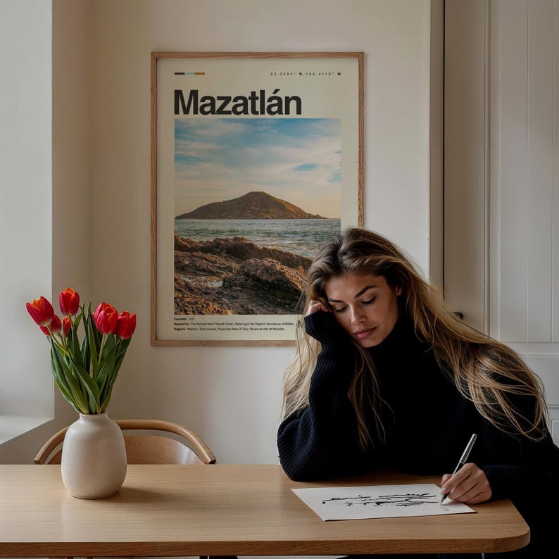 May include: A woman sits at a wooden table, drawing on a white sheet of paper with a black pen. A framed poster with the text "Mazatl&aacute;n" and a picture of a beach scene hangs on the wall behind her. A vase with red tulips sits on the table in front of her.