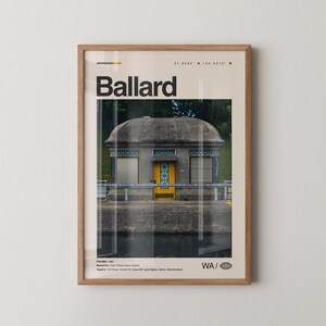 May include: A framed print featuring the word "Ballard" in bold black letters. The image within the frame showcases a concrete building with a yellow door and a domed roof. The print includes coordinates and the abbreviation "WA".