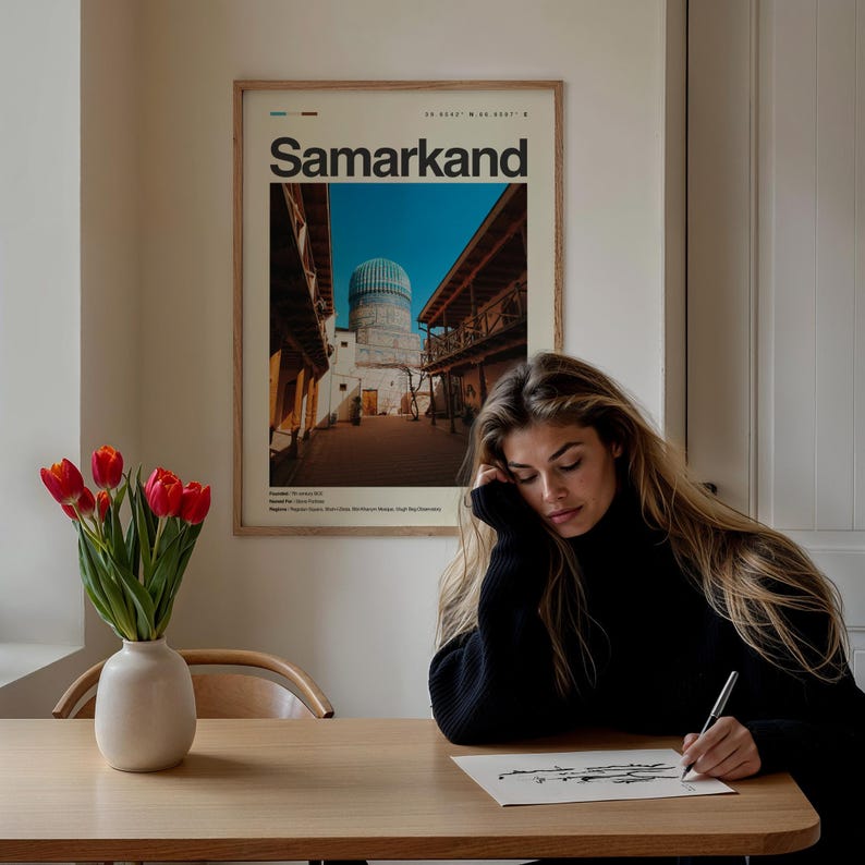 May include: A framed poster with the word "Samarkand" in a minimalist design hangs on a wall. The poster features a photograph of a building with a blue dome. A vase of red tulips sits on a wooden table.