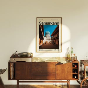 May include: A framed poster with the word "Samarkand" in large text, depicting a street scene with a blue-domed building. The poster is displayed above a wooden cabinet with a record player and bottles.