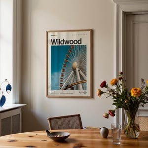 May include: A framed poster featuring a photograph of a Ferris wheel against a blue sky. The poster has the word "Wildwood" at the top and "NJ" at the bottom. The poster is in a room with a wooden table and a vase of flowers.