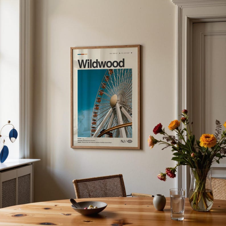 May include: A framed poster featuring a photograph of a Ferris wheel against a blue sky. The poster has the word "Wildwood" at the top and "NJ" at the bottom. The poster is in a room with a wooden table and a vase of flowers.