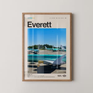 May include: A framed poster with the word "Everett" in black. The poster shows aeroplanes on a tarmac with a blue sky. The poster is in a wooden frame. The poster includes the coordinates 47.9780° N, 122.2021° W.