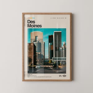 May include: A framed print featuring a cityscape of Des Moines, Iowa, with a retro-style design. The print includes the city's name in bold letters, coordinates, and other details. The image showcases a vibrant urban scene with tall buildings and a bright blue sky.