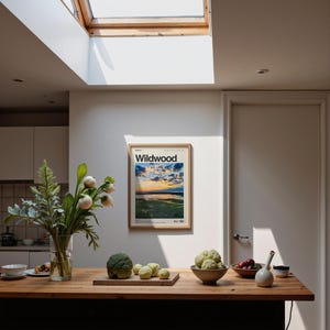 May include: A kitchen scene with a wooden countertop and a framed poster that reads "Wildwood." The poster features a landscape with a sunset. A vase of flowers, a cutting board with vegetables, and a bowl of fruit are on the counter.