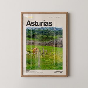 May include: A framed print featuring the word "Asturias" in bold black letters. The image shows a scenic landscape with green hills, a cow, and a wooden fence. The print includes the text "ESP" and a globe icon.