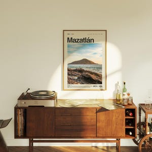 May include: A vintage-style wooden cabinet with a record player on top. The cabinet has three drawers and a shelf for storing records. A poster with the text "Mazatl&aacute;n" and a picture of a beach scene is hanging on the wall behind the cabinet.