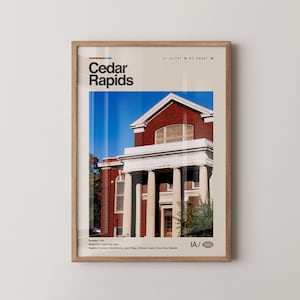 Puede incluir: Impresión enmarcada que presenta una fotografía de un edificio de ladrillo con columnas blancas y un cielo azul. La impresión incluye el texto "Cedar Rapids" y las coordenadas de la ciudad. La impresión está en un marco de madera.
