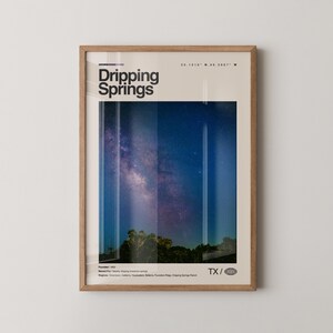 May include: A framed art print featuring the words "Dripping Springs" in black text. The image showcases a night sky with the Milky Way above a dark treeline. The print includes the coordinates 30.1016° N, 98.0807° W and the letters TX.