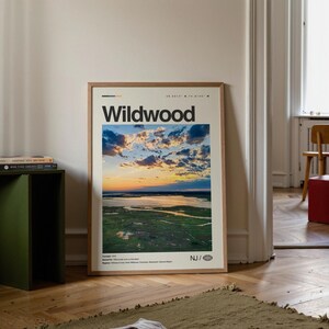 May include: A framed print featuring the word "Wildwood" in bold black letters. The image within the frame depicts a scenic aerial view of a coastal landscape at sunset, with a vibrant sky and calm water.