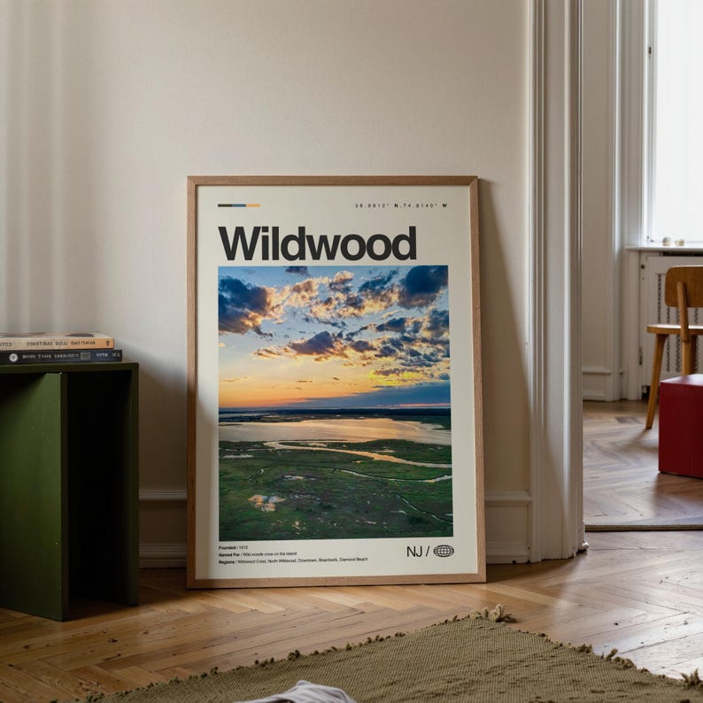 May include: A framed print featuring the word "Wildwood" in bold black letters. The image within the frame depicts a scenic aerial view of a coastal landscape at sunset, with a vibrant sky and calm water.