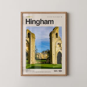 May include: A framed print featuring the word "Hingham" in bold black letters. The image within the frame showcases a historic building with two tall, weathered stone structures framing a view of a building and blue sky. The print is in a light wood frame.