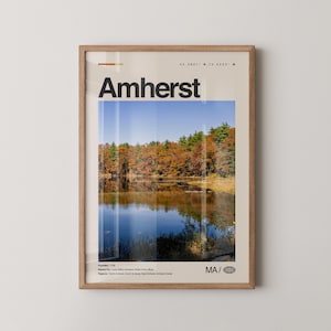 Könnte beinhalten: Ein gerahmter Kunstdruck mit dem Wort "Amherst" in Schwarz über einer Landschaftsszene. Das Bild zeigt einen See, der Herbstbäume unter blauem Himmel reflektiert. Der Druck enthält Koordinaten und die Abkürzung "MA".
