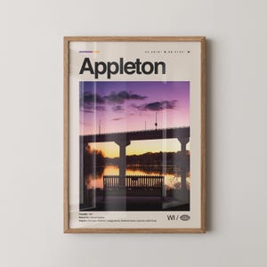 Puede incluir: Impresión enmarcada que presenta una vista panorámica de Appleton, Wisconsin, con un puente sobre un río al atardecer. La impresión incluye el nombre de la ciudad, coordenadas y una lista de regiones. La paleta de colores incluye morado, naranja y beige.