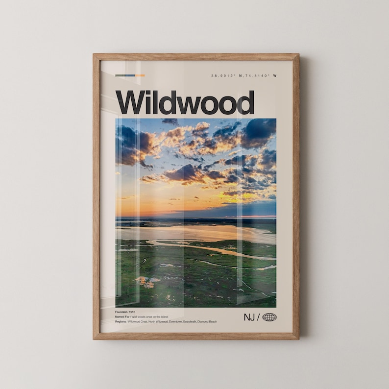 May include: A framed print featuring the word "Wildwood" in bold black letters. The image within the frame showcases a scenic aerial view of a coastal landscape at sunset, with a vibrant sky and green marshland. The print includes text indicating the location's coordinates and founding year.