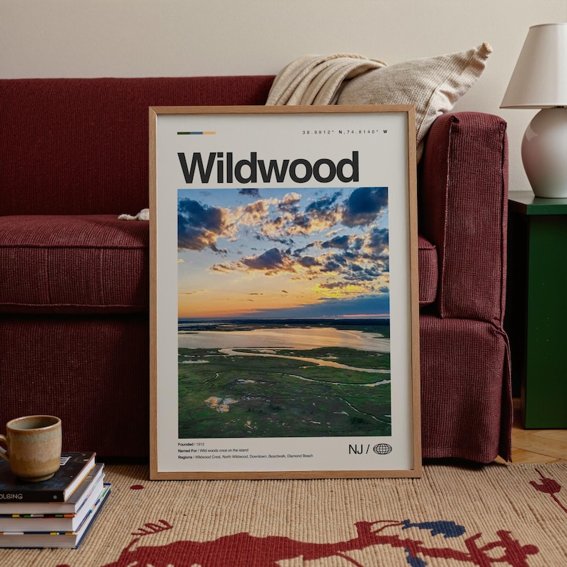 May include: A framed Wildwood print featuring a scenic aerial view of a coastal landscape at sunset. The print has a wooden frame and includes the text "Wildwood" in bold black letters. The image captures a vibrant sky with clouds and a body of water.
