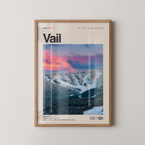 Könnte beinhalten: Ein gerahmtes Poster mit dem Wort 'Vail' in fetten schwarzen Buchstaben, das eine schneebedeckte Berglandschaft zeigt. Das Bild zeigt einen lebendigen Sonnenuntergang mit rosa und orangen Farbtönen. Das Poster enthält die Koordinaten 39.6403° N, 106.3742° W.