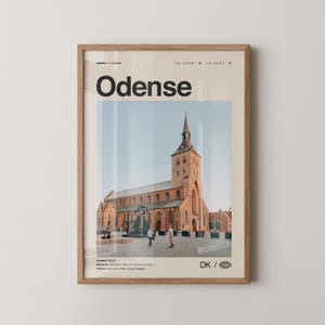 May include: A framed print featuring the word "Odense" in bold black letters above a photograph of a large brick church with a tall steeple. The print includes coordinates and the letters "DK" with a globe icon.