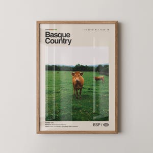 May include: Framed poster featuring a pastoral scene in the Basque Country. The image shows a brown cow in a green field, with the text "Basque Country" at the top. The poster is in a wooden frame.