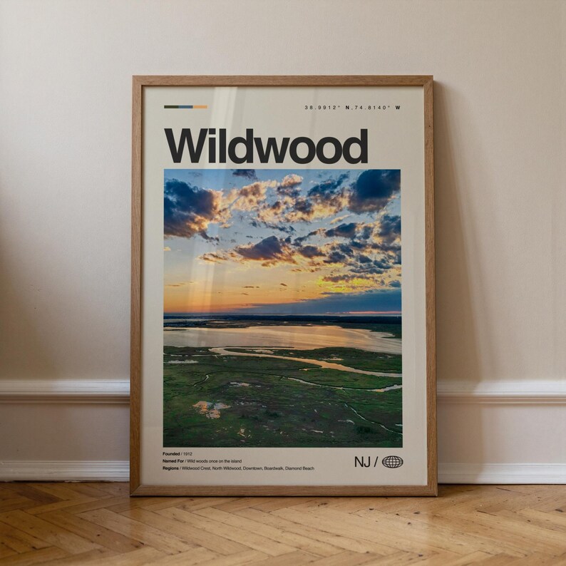 May include: Framed poster featuring the word "Wildwood" in bold black letters above a scenic landscape. The image showcases a sunset over a body of water and marshland. The poster includes the text "NJ /" and coordinates.