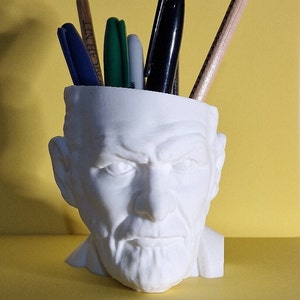 Può includere: Busto in ceramica bianca di un uomo con la barba, utilizzato come organizzatore da scrivania. Il busto ha una testa vuota, che contiene una varietà di penne e matite.