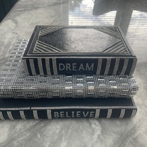 May include: Three black decorative boxes with silver glitter accents. The top box says "DREAM", the middle box has a silver glitter pattern, and the bottom box says "BELIEVE".