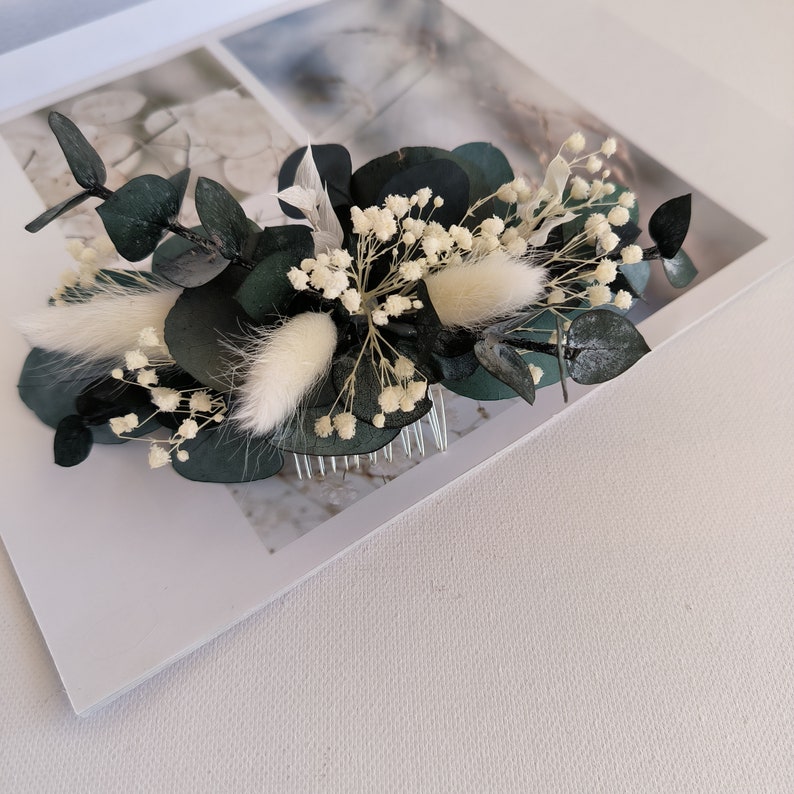 May include: A dark green eucalyptus and white baby's breath floral hair comb. The comb is decorated with white fluffy sprigs and small white flowers.