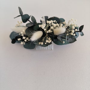 May include: A hair comb with a floral design featuring white dried flowers and dark green eucalyptus leaves.